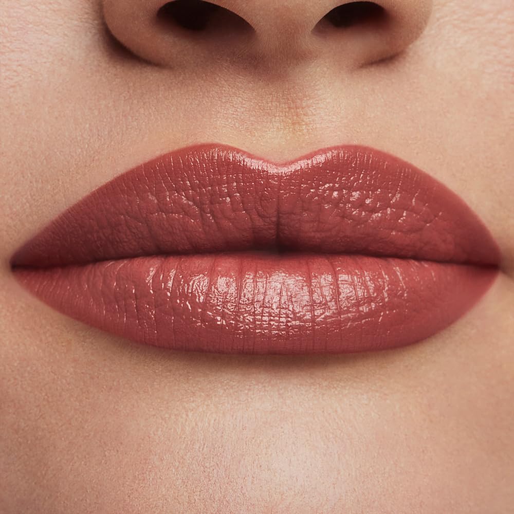 Estée Lauder lipstick beside common objects showing compact size and travel readiness