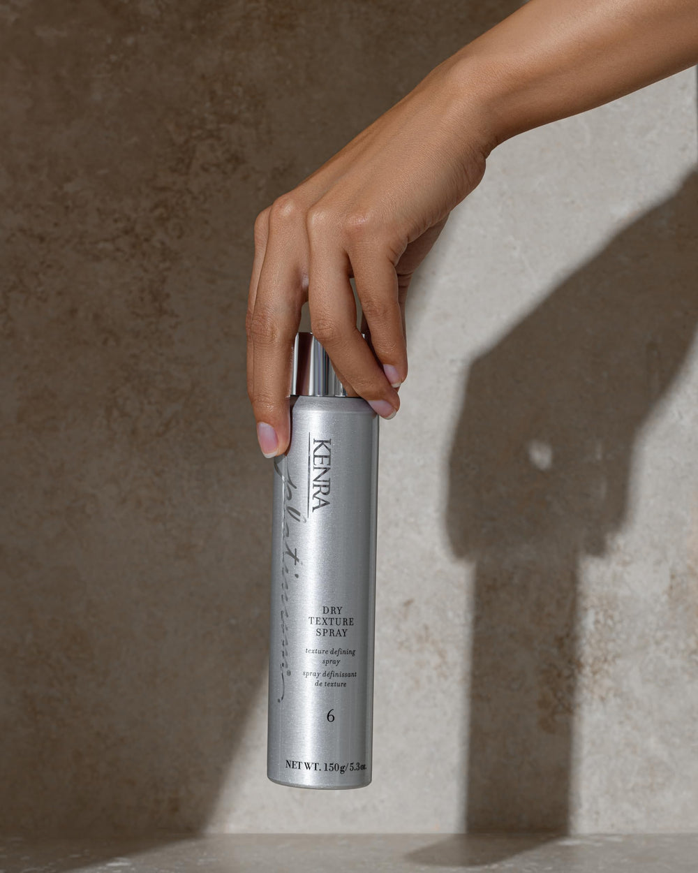 Kenra bottle in hand showing scale and travel-friendly size for on-the-go styling