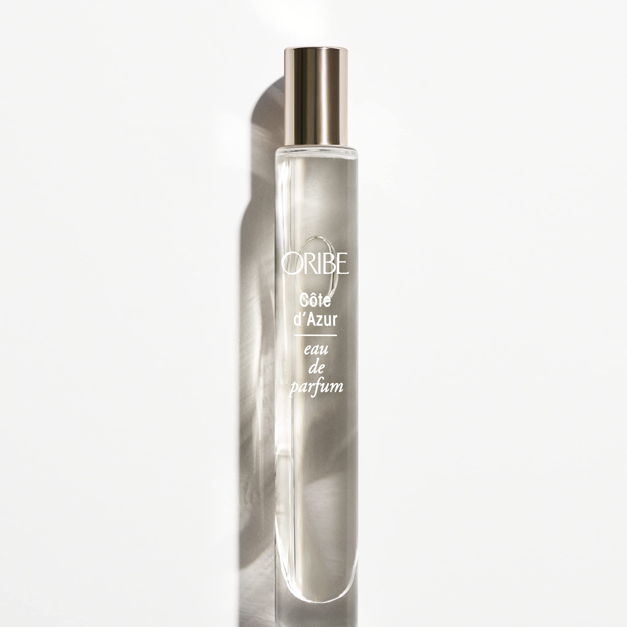 ORIBE atomizer in hand beside passport demonstrating travel-friendly convenience