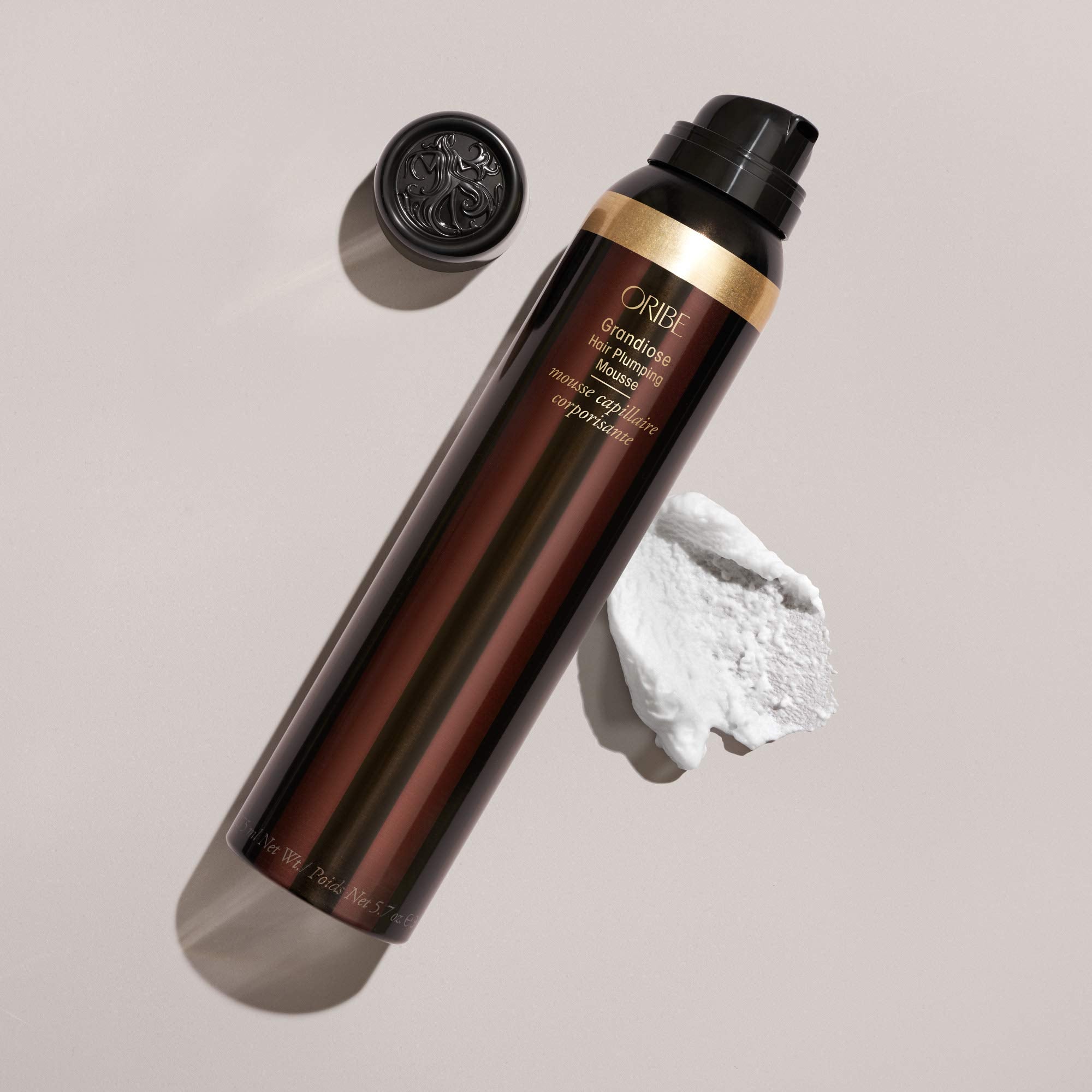 Oribe Grandiose placed beside a hand to show 5.7oz size and portability