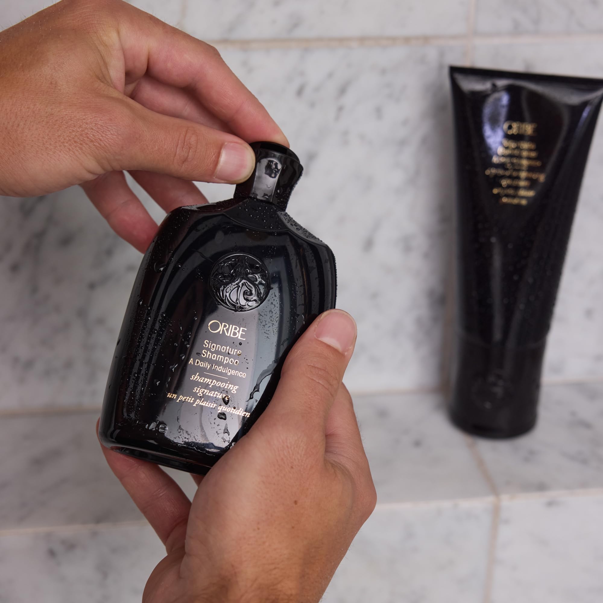 Oribe conditioner next to hand for scale, showing the 6.8oz travel-friendly size