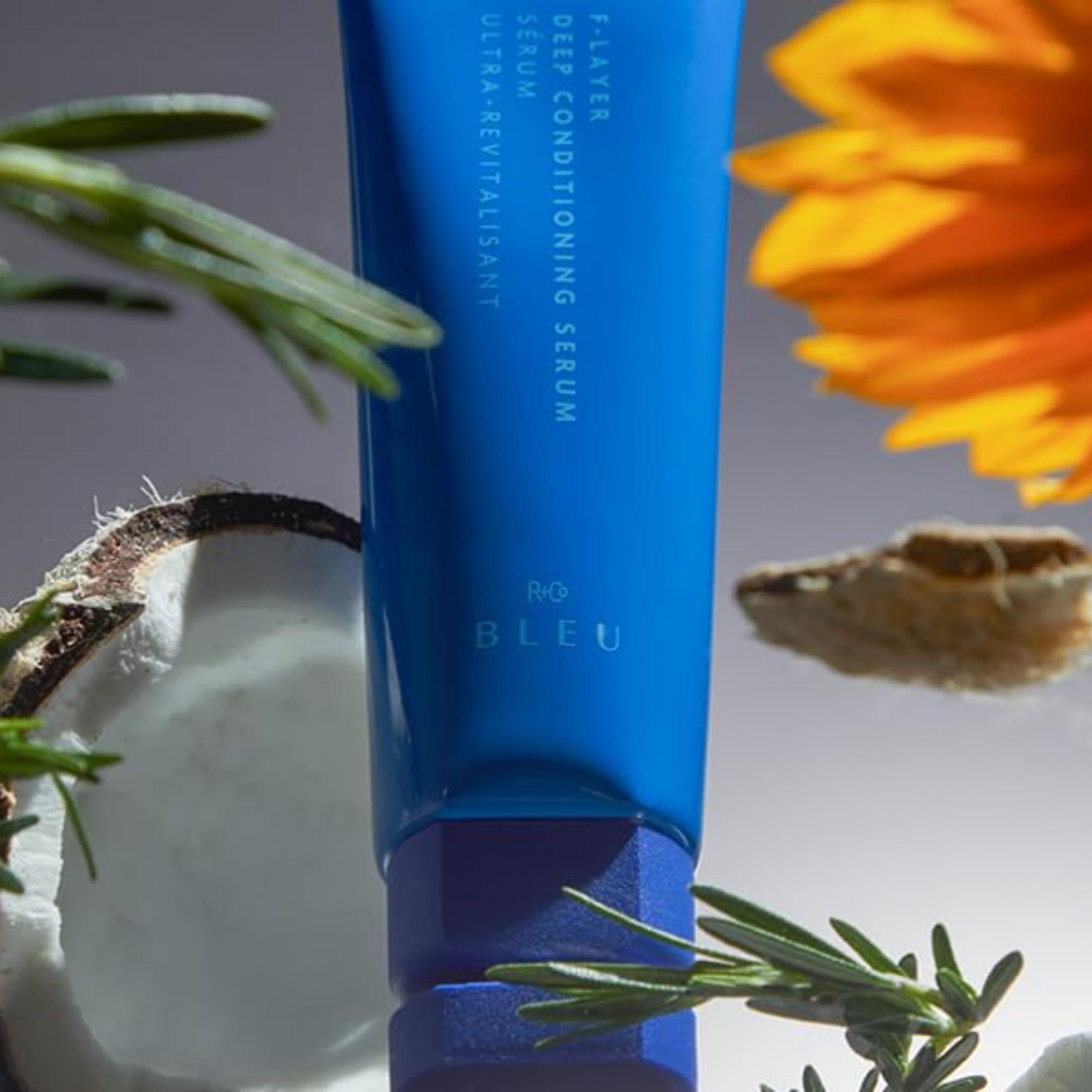 R+Co BLEU F‑Layer next to common items to show 4.2 oz size and travel convenience