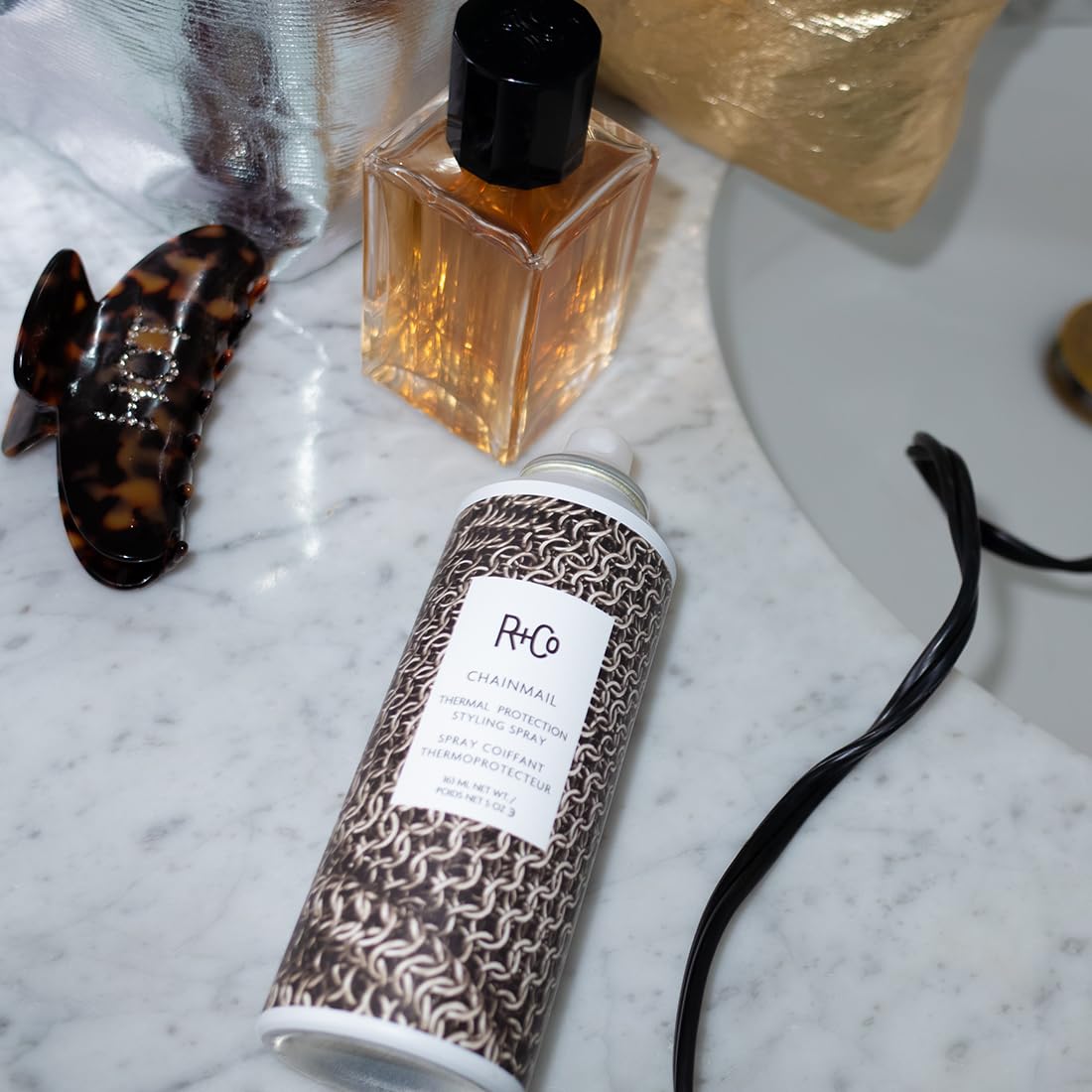 R+Co CHAINMAIL bottle next to a hand for scale, compact 5 oz travel-friendly benefit