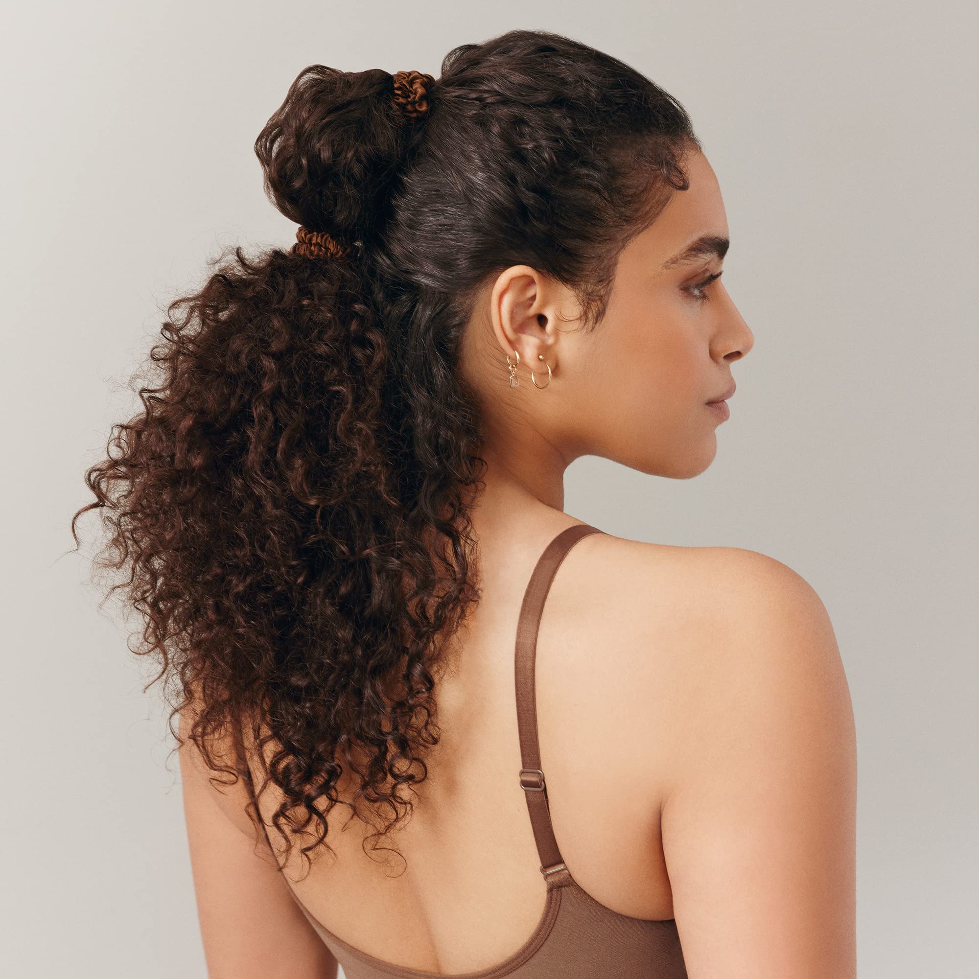 SLIP scrunchie beside fingers to show slim size and discreet styling benefit