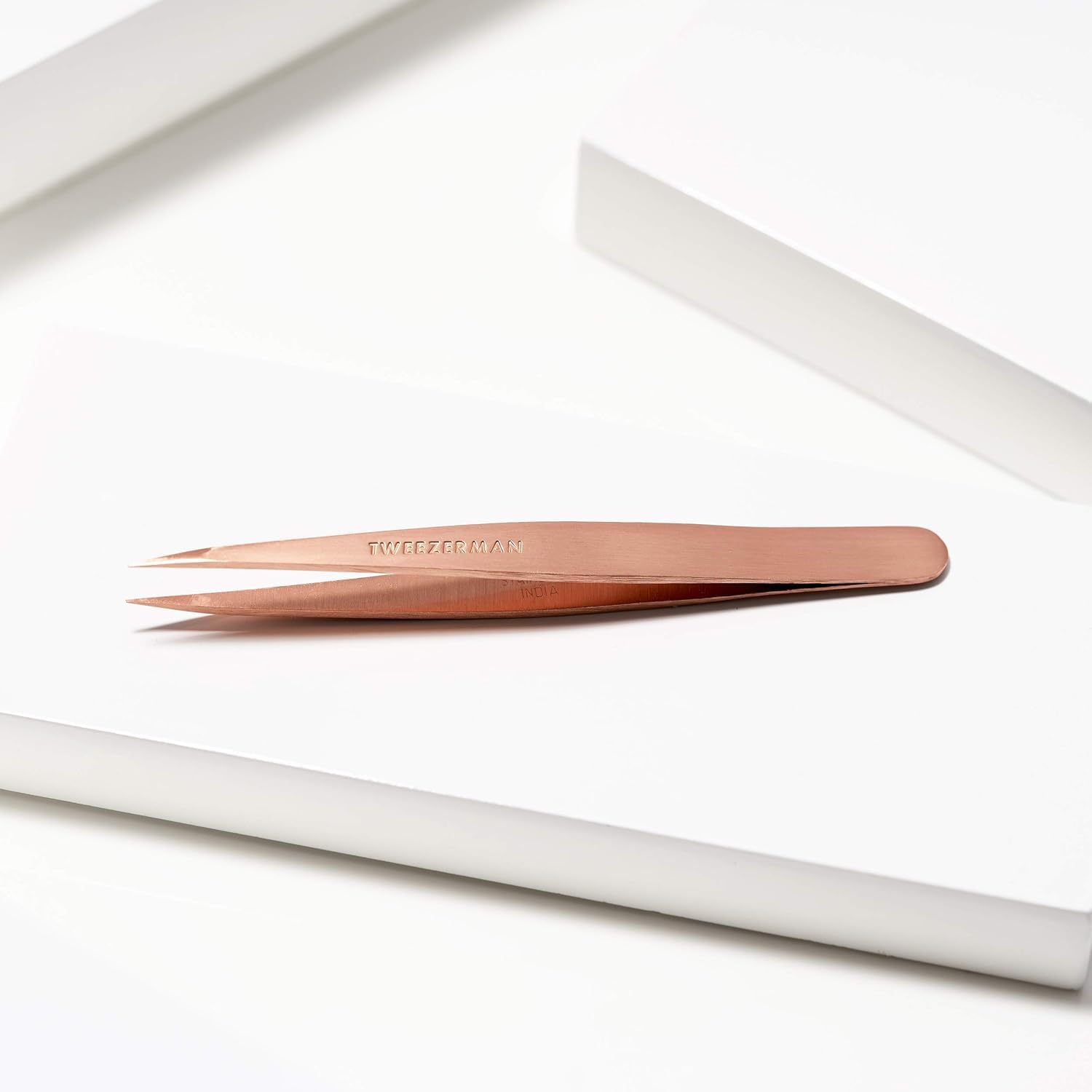 Tweezerman tweezer beside coin for scale showing convenient handheld size